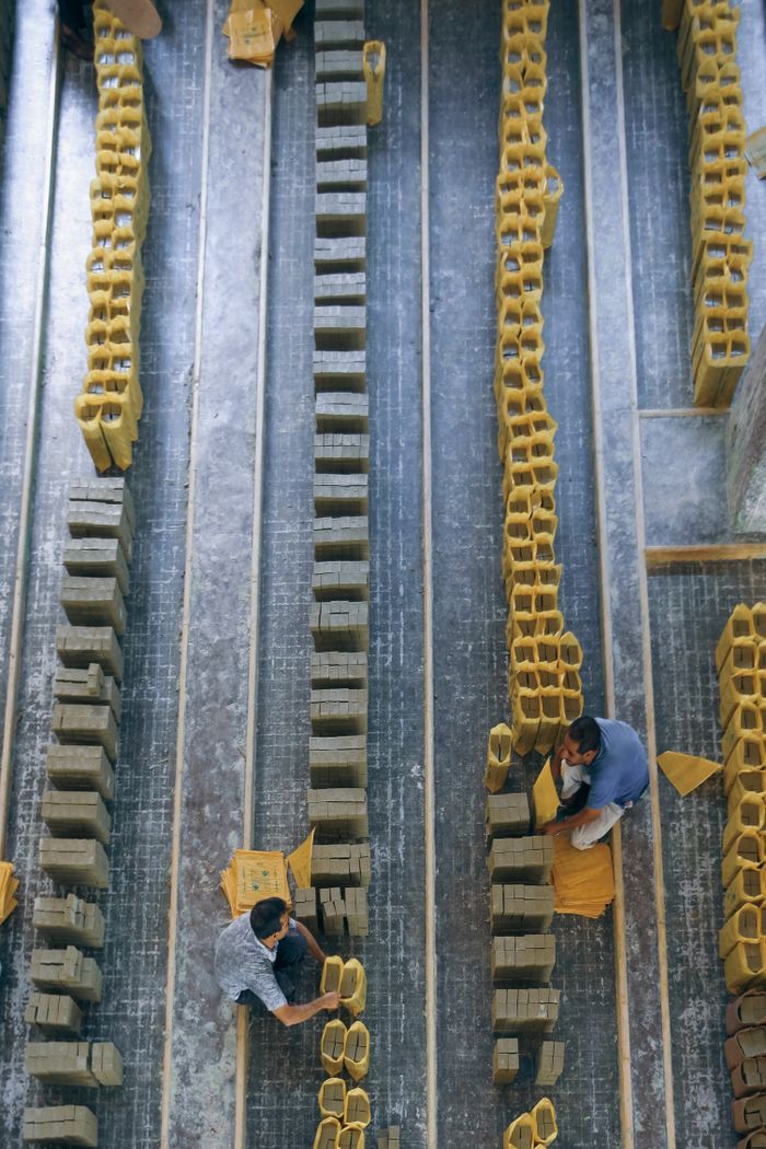 Top angle view of two men arranging rows of clay bricks in an industrial setting.